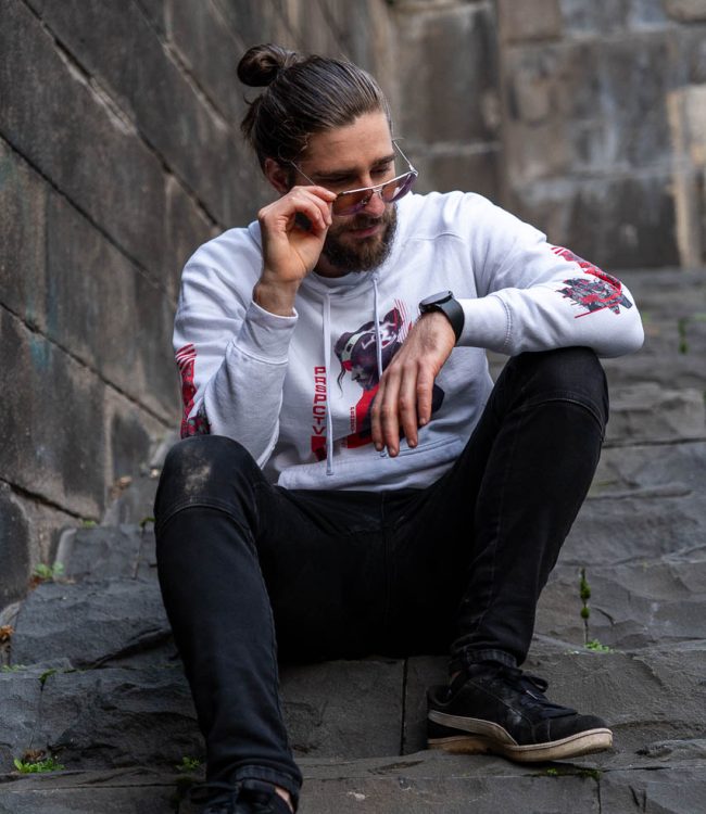 Mike Bello sitting on a set of stairs in the city wearing a white B-Side hoodie and sunglasses