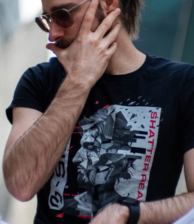 Mike Bello close-up sitting in the city wearing a black B-Side T-shirt and sunglasses